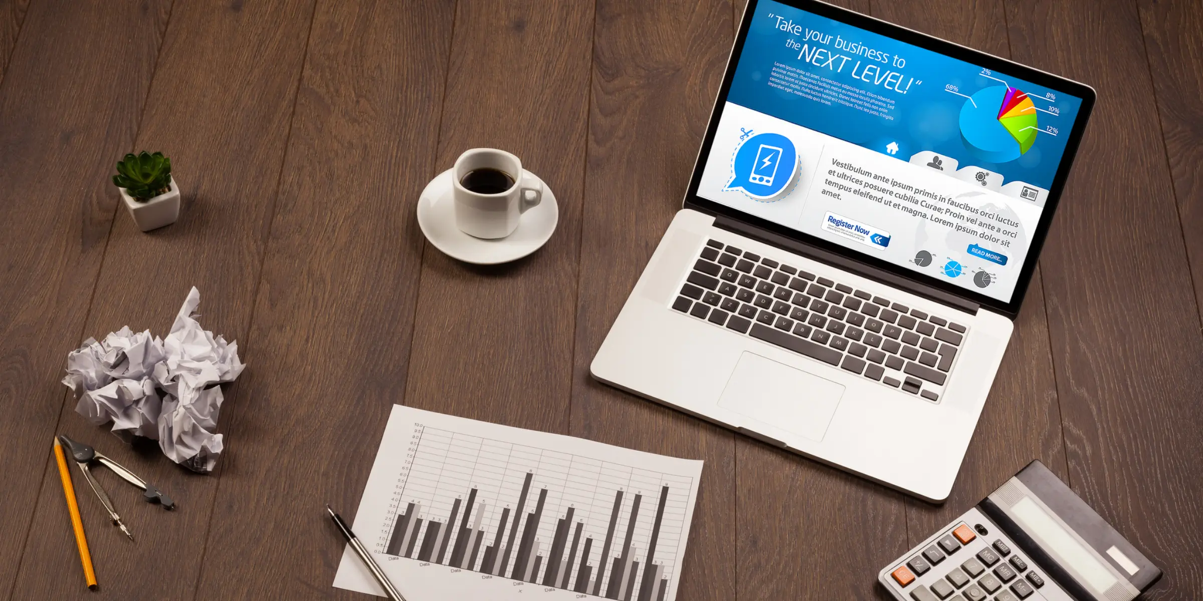 A laptop is sitting on a wooden desk with a calculator and a pen.