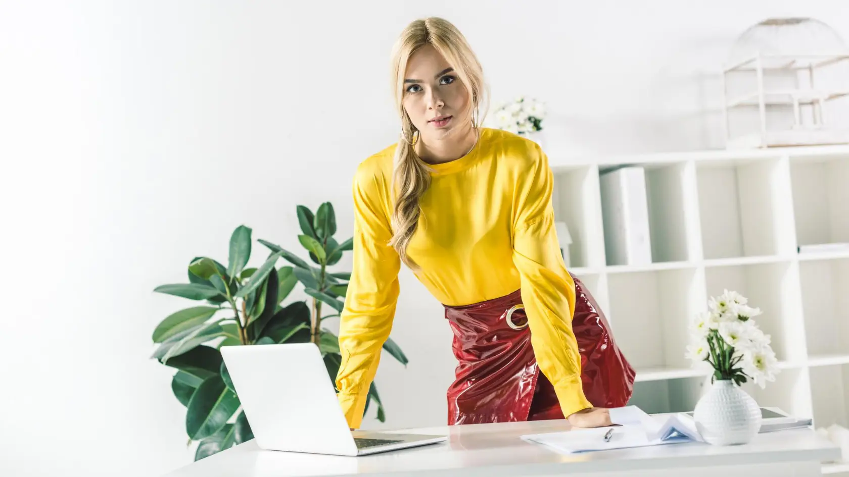 A woman in a yellow shirt is sitting at a desk with a laptop.