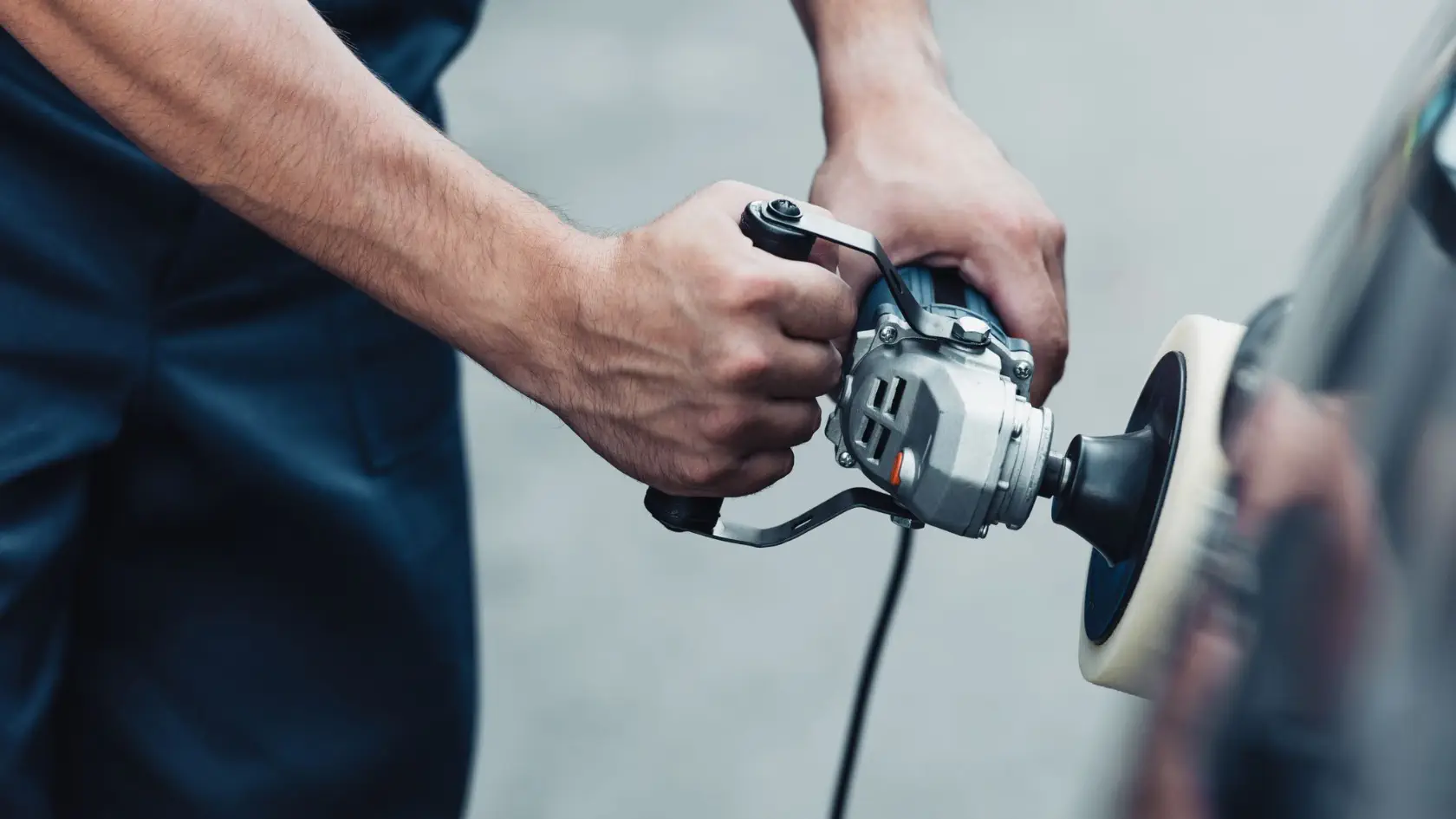 A man is sanding a car with a tool.