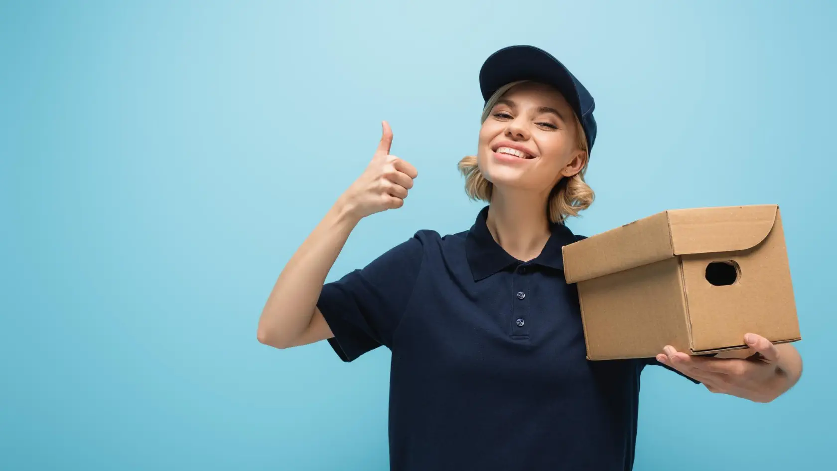 A woman holding a cardboard box and giving the thumbs up.