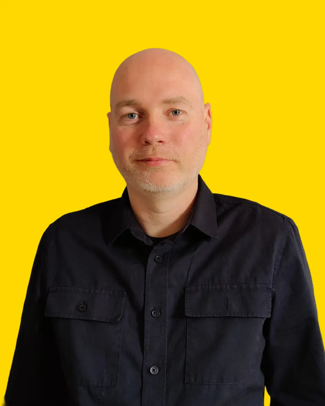 A bald man wearing a black shirt stands in front of a bright yellow background.